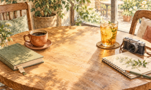 カフェのテーブルに並ぶコーヒーカップと冷たいお茶のグラス。本とカメラが離して置かれている